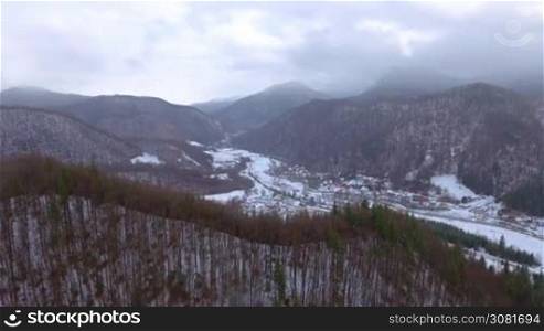 Snow falling on small village in the mountains. Winter panorama. Aerial video