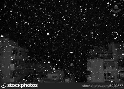 Snow falling over city buildings at night. Black and white.