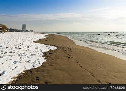 Snow in the sand. Seascape with snow on the beach and tower in the background