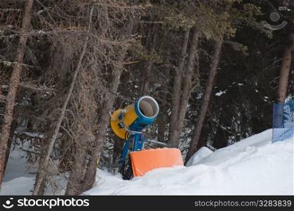 Snow making machine located at the border of the skiing slope in front of a forest. Shot in Livigno, Italian Alps