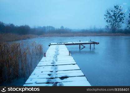 Snow on a wooden pier on the lake shore, view on a foggy December day, Stankow, Poland