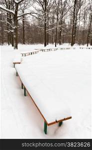 snow on benches in city park in winter