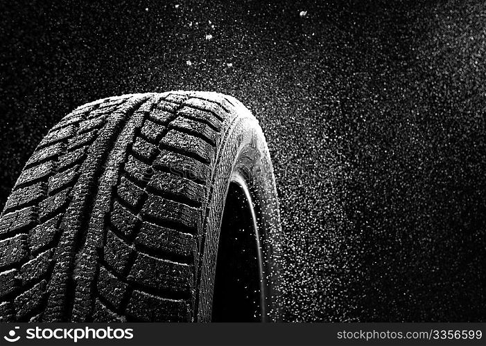 Snow sweeps up a winter tyre cover on a black background
