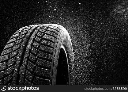 Snow sweeps up a winter tyre cover on a black background