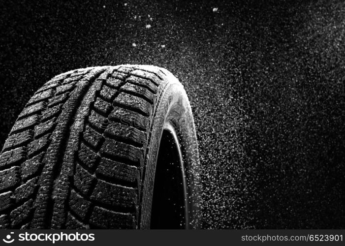 Snow sweeps up a winter tyre cover on a black background. Rubber in snow