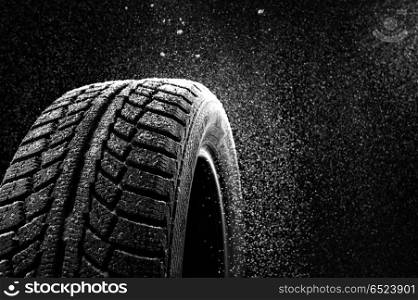 Snow sweeps up a winter tyre cover on a black background. Rubber in snow