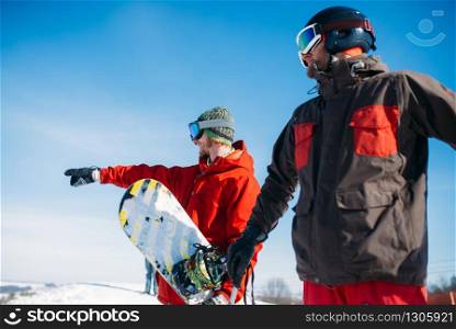Snowboarder and skier poses on the top of mountain, blue sky on background. Winter active sport, extreme lifestyle, snowboarding and skiing