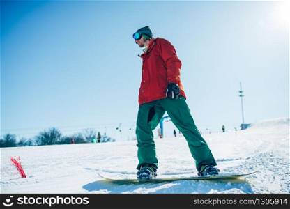Snowboarder in glasses poses with board in hands, blue sky and snowy mountains on background. Snowboarder in glasses poses with board in hands
