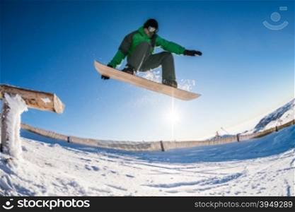 Snowboarder jumping from a wood rail against blue sky.
