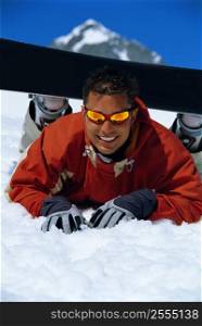 Snowboarder lying on snowy hill wearing board and smiling (selective focus)