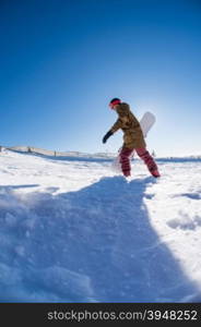 Snowboarder walking through deep fresh snow against blue sky.