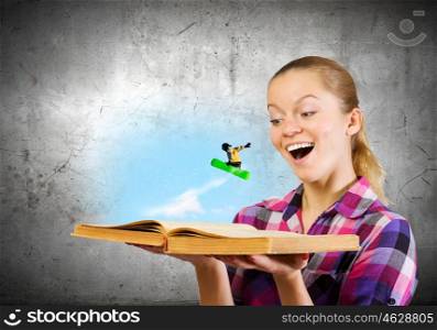 Snowboarding concept. Young woman looking in opened book and snowboarder making jump