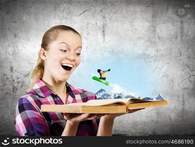 Snowboarding concept. Young woman looking in opened book and snowboarder making jump