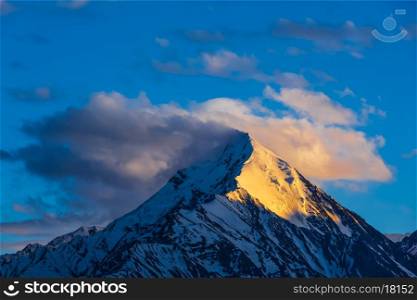 Snowcapped summit top of mountain in Himalayas in clouds on sunset. Himachal Pradesh, India