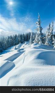 Snowdrifts on winter snow covered mountainside, fir trees on hill top, and blue sunshiny sky