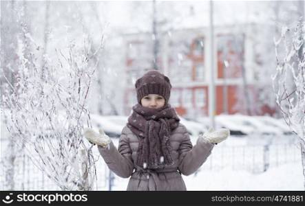 Snowfall, portrait of a happy little girl on the background of a winter park