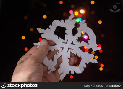 Snowflake shaped paper in hand on bokeh light background