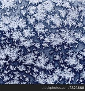 snowflakes and frost on frozen window glass in cold winter evening close up