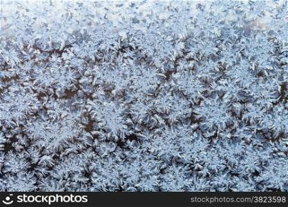 snowflakes and frost pattern on frozen window in cold winter evening