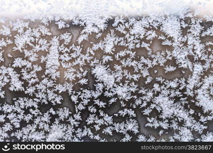 snowflakes and frost pattern on window pane in cold winter evening