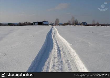 Snowmobile track towards the village, winter sunny day