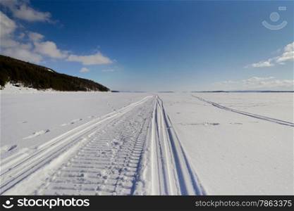 Snowmobile trail stretching into the distance against the blue sky and snowy expanses