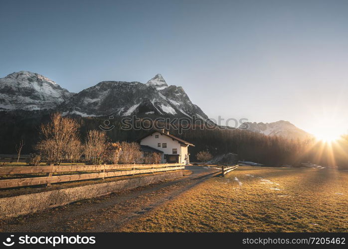 Snowy Alps mountains peaks and Austrian farm in the evening light, on a sunny day of winter, in Ehrwald, Austria. December sunset scenery.