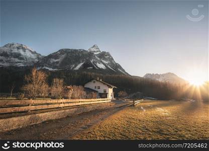 Snowy Alps mountains peaks and Austrian farm in the evening light, on a sunny day of winter, in Ehrwald, Austria. December sunset scenery.