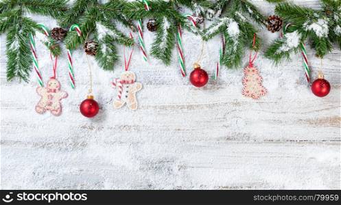 Snowy Christmas evergreen branches with hanging ornaments on rustic white wood background