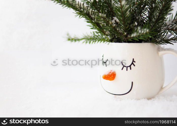 snowy fir branches in a cup with the face of a sleeping snowman on a white background. copy space.