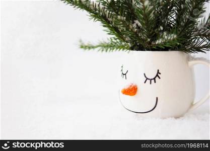 snowy fir branches in a cup with the face of a sleeping snowman on a white background. copy space.