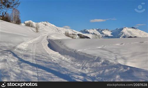 snowy footpath crossing alpine mountain under blue sky