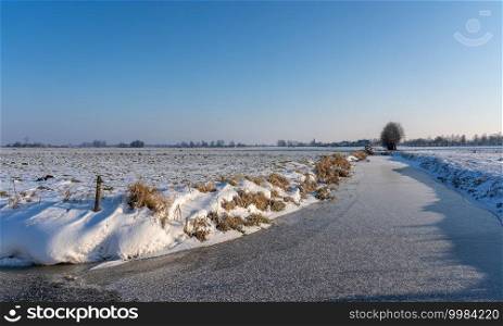 Snowy landscape with a frozen ditch under a sunny sky