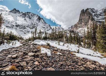 Snowy landscape with rocks and mountains in snow around at autumn with cloudy sky. Rocky Mountain National Park in Colorado, USA.