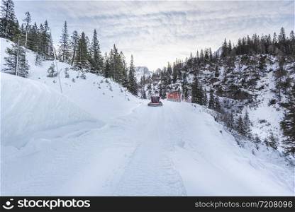 Snowy road in the Austrian mountains. Winter scenery with snow-covered road and snowdrifts on the roadside. Snow groomer cleaning the road