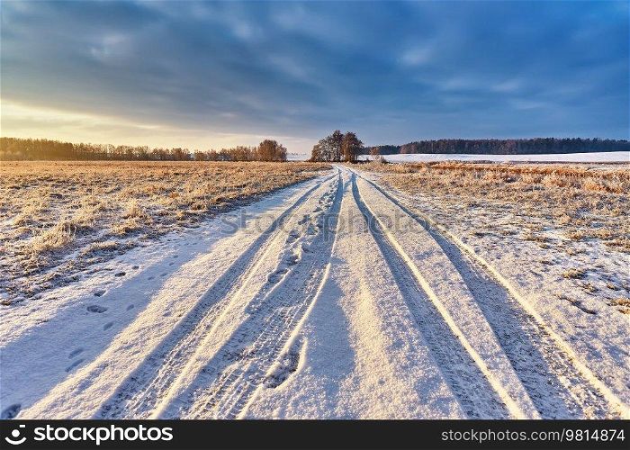 Snowy rural road with traces and footprints on winter riverbank. Frost on grass, cane. February Forest river sunrise. Cold Weather landscape. Europe rural scene. Low Cloudy sky