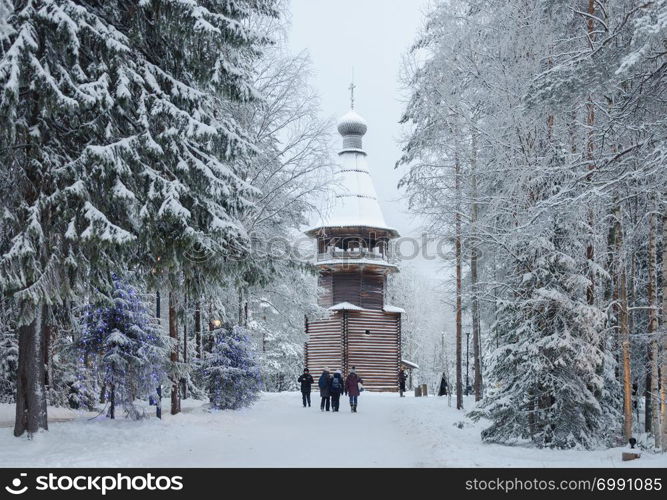 Snowy trees, walking people near ancient wooden belfry (1854) in the open air museum Malye Korely near Arkhanglesk, Russia. Winter time.