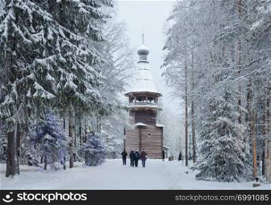 Snowy trees, walking people near ancient wooden belfry (1854) in the open air museum Malye Korely near Arkhanglesk, Russia. Winter time.
