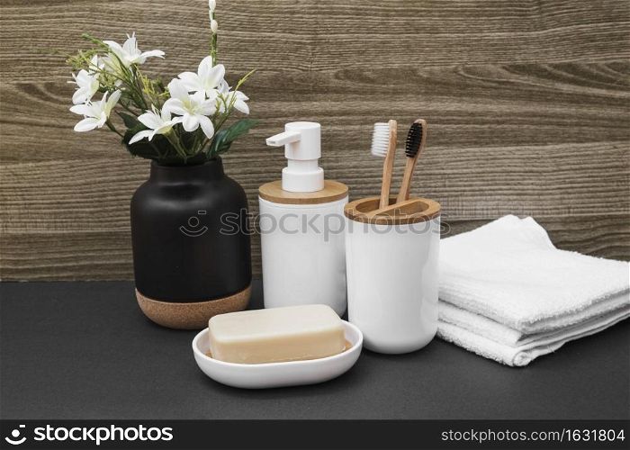 soap toothbrush cosmetic bottle towel white flower vase black surface