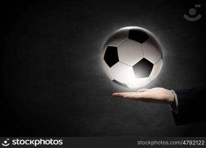 Soccer ball in palm. Hand of businessman on dark background holding soccer ball