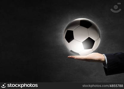 Soccer ball in palm. Hand of businessman on dark background holding soccer ball