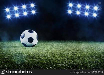 Soccer ball on a football field backlit by two banks of eight bright shining spotlights in a grass level view with mist