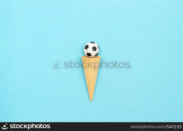 Soccer or football ball in ice cream waffle cone on blue paper background in minimal style. Concept sports entertainment. Top view Copy space Template for text or your design.. Soccer or football ball in ice cream waffle cone on blue background in minimal style. Concept sports entertainment. Top view Copy space Template for text or your design