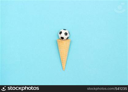Soccer or football ball in ice cream waffle cone on blue paper background in minimal style. Concept sports entertainment. Top view Copy space Template for text or your design.. Soccer or football ball in ice cream waffle cone on blue background in minimal style. Concept sports entertainment. Top view Copy space Template for text or your design