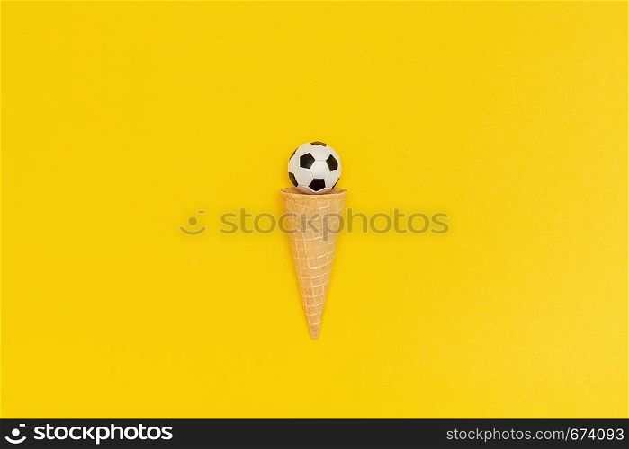 Soccer or football ball in ice cream waffle cone on yellow paper background in minimal style. Concept sports entertainment. Top view Copy space Template for text or your design.. Soccer or football ball in ice cream waffle cone on yellow background in minimal style. Concept sports entertainment. Top view Copy space Template for text or your design