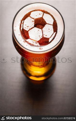 soccer or football ball symbol on foam in beer glass on black table, view from above
