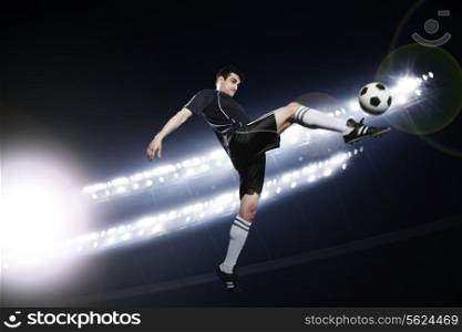 Soccer player in mid air kicking the soccer ball, stadium lights at night in background