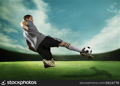 Soccer player kicking the soccer ball in mid air, in the stadium with the sky
