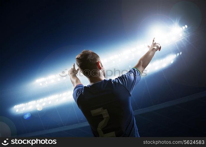 Soccer player with arms raised cheering, stadium at night time