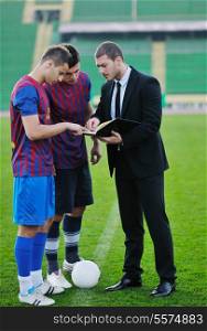soccer sport manager in business suit coach and football player on stadium with green grass and white ball